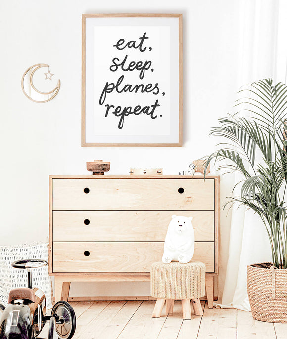 Hand lettered phrase 'eat, sleep, planes, repeat' artwork hangs in a neutral, scandi style kids bedroom