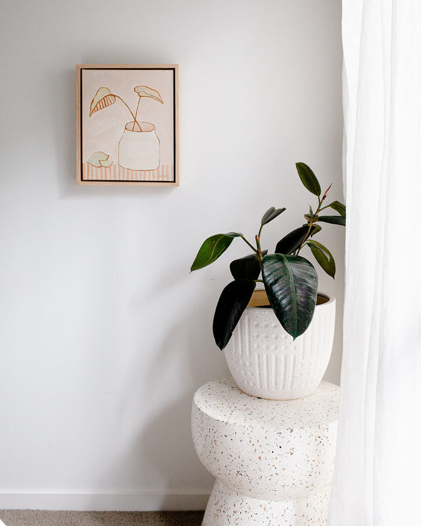 Boho style artwork of two leaves in a vase in neutral tones, styled in a light and bright modern room with terrazzo stool
